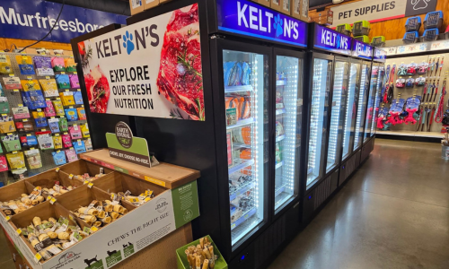 Pet store aisle with a Kelton’s freezer section displaying pet food. Nearby, boxes of chew treats are stacked. Vibrant pet supplies line the walls.